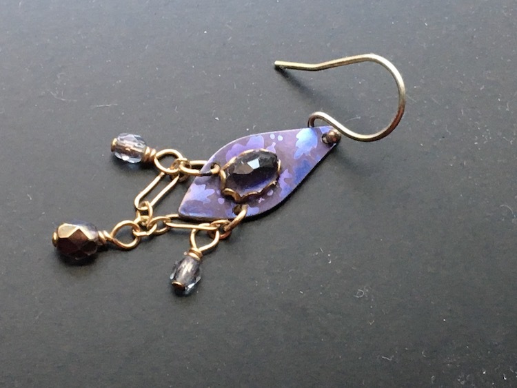 An oval, purple earring with gold chains