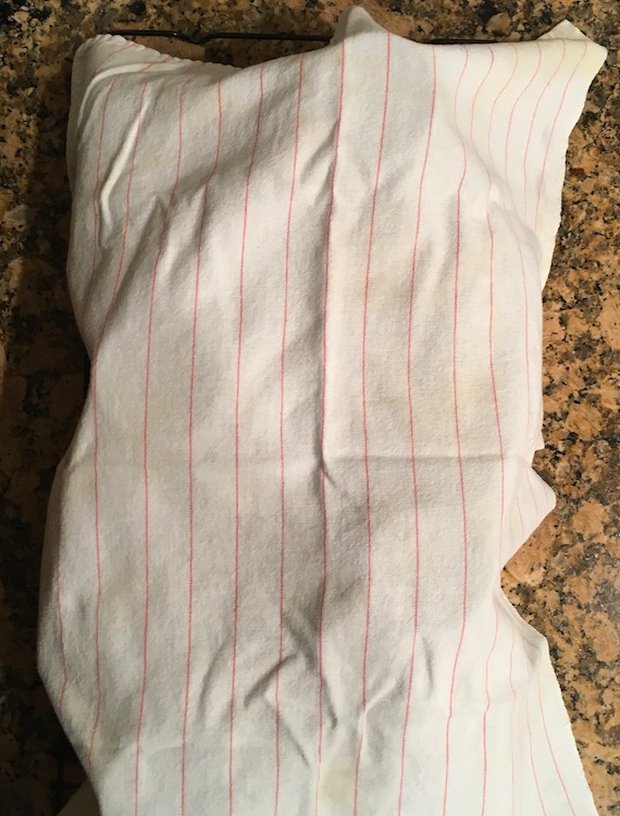 Photo of a white dishtowel with thin red stripes draped over loaves of pumpkin bread
