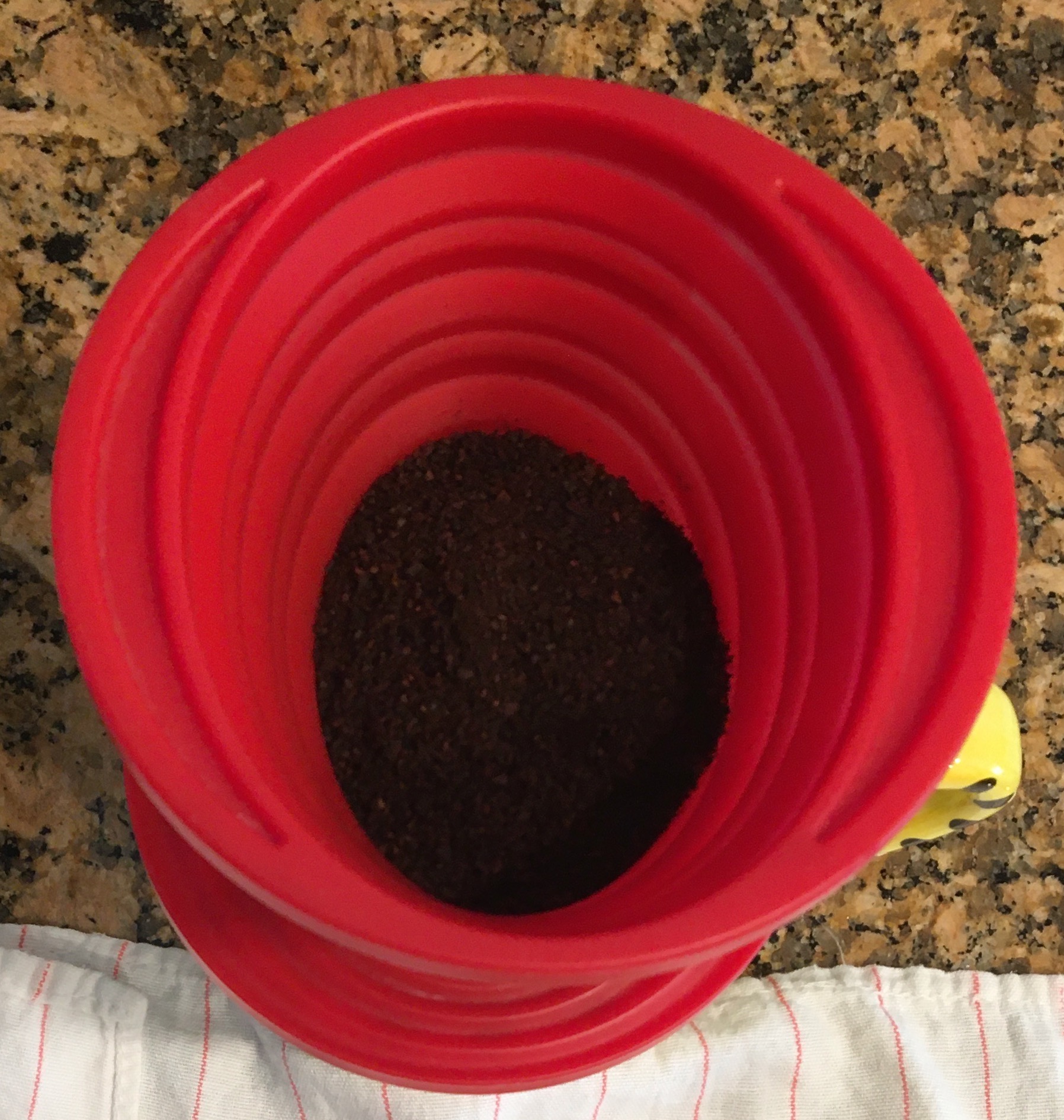 Photo of a red, silicon coffee filter containing coffee grounds.
