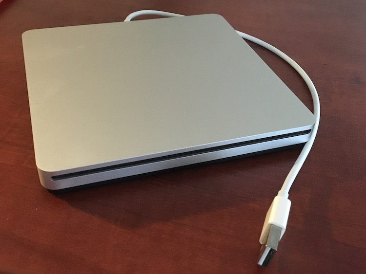 Photo of a square, silver external DVD player and the white USB cord attached to the back of it