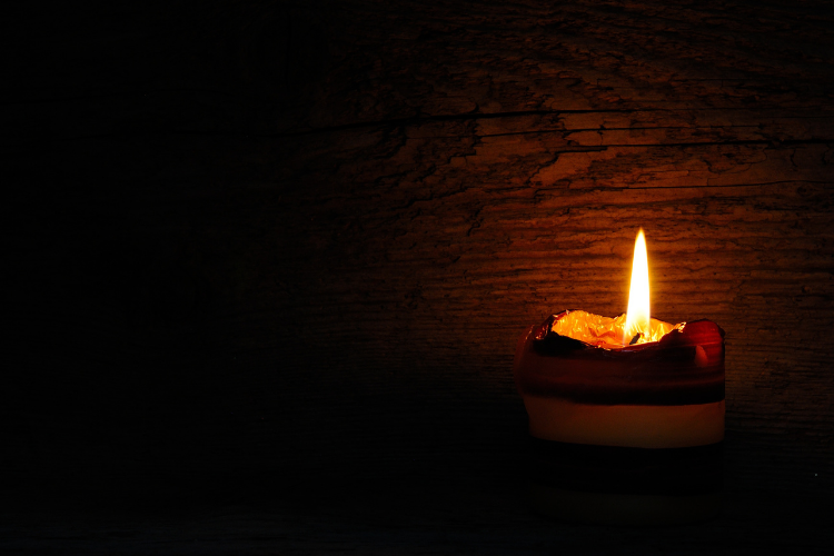 Photo of a dark background with a squat candle on the right providing a bit of illumination