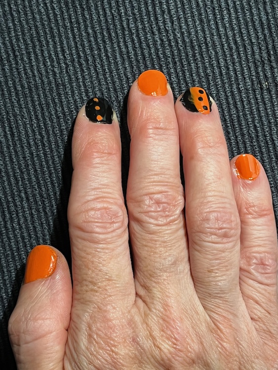 A photo of a right hand with fingernails painted orange or black with an orange design for Halloween